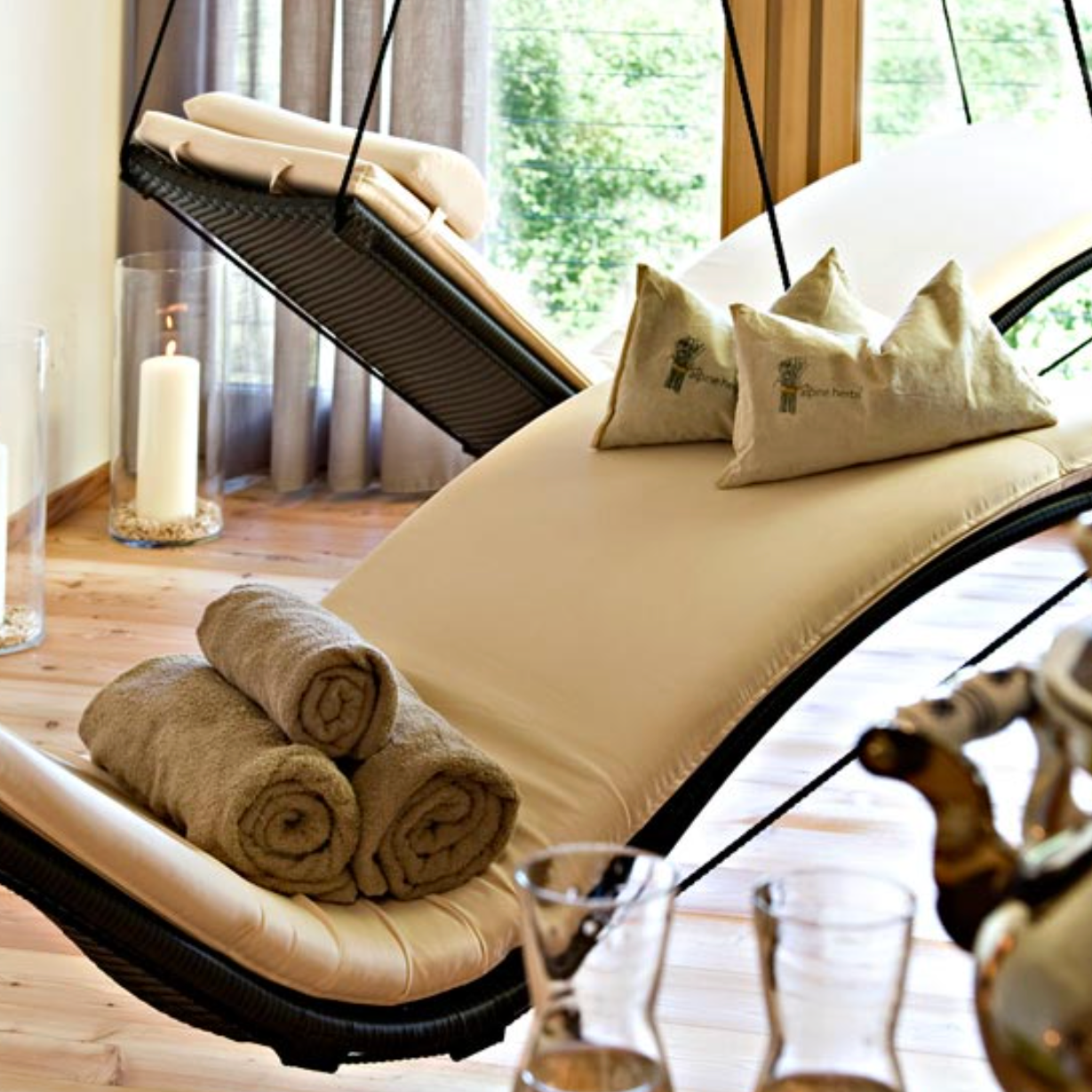 Beige lounge chair with rolled towels in a room with large windows.