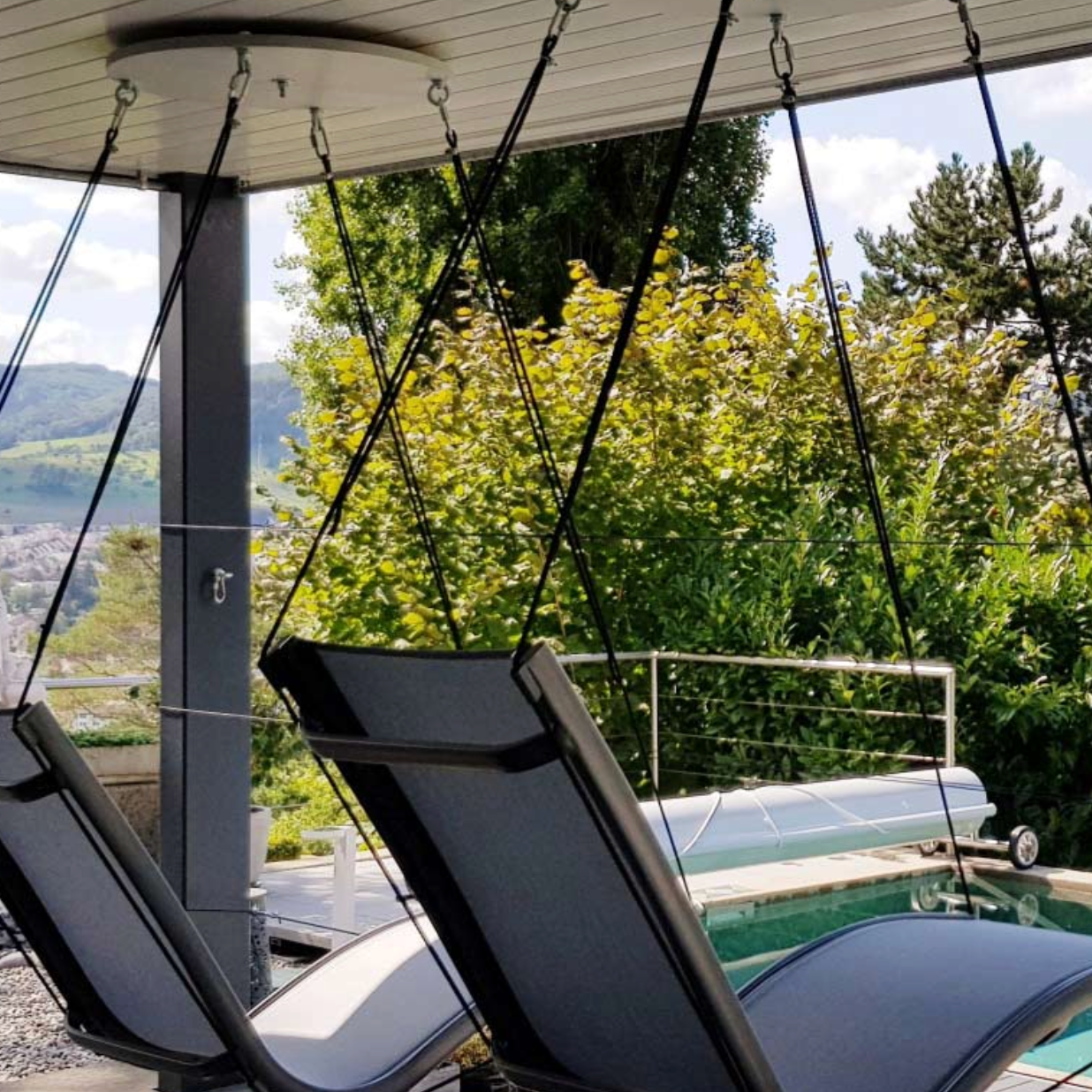 Two black hanging chairs by a pool with a scenic view of trees and mountains.