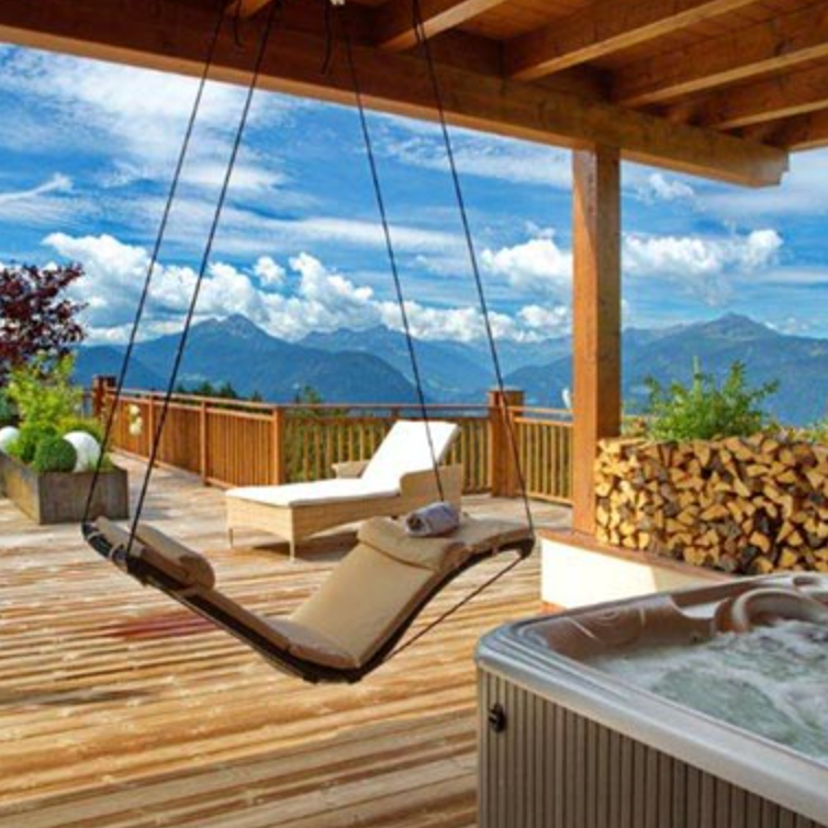 Wooden deck with a swing, lounge chair, and hot tub overlooking mountains.