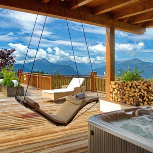 Wooden deck with a swing, lounge chair, and hot tub overlooking mountains.